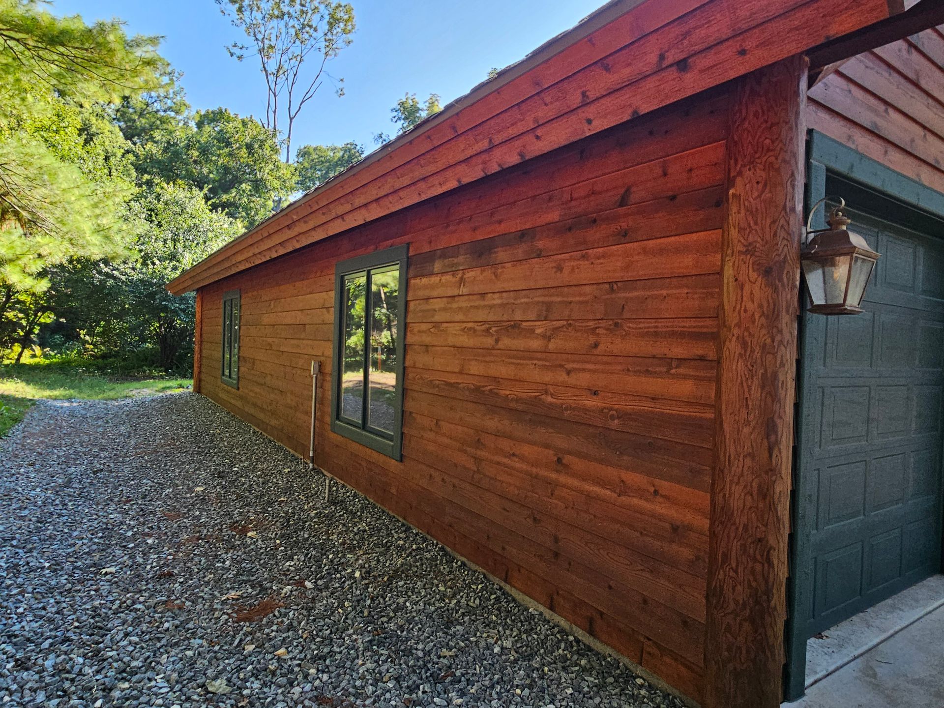 Wooden building with dark trim, windows, and garage door. Gravel driveway.