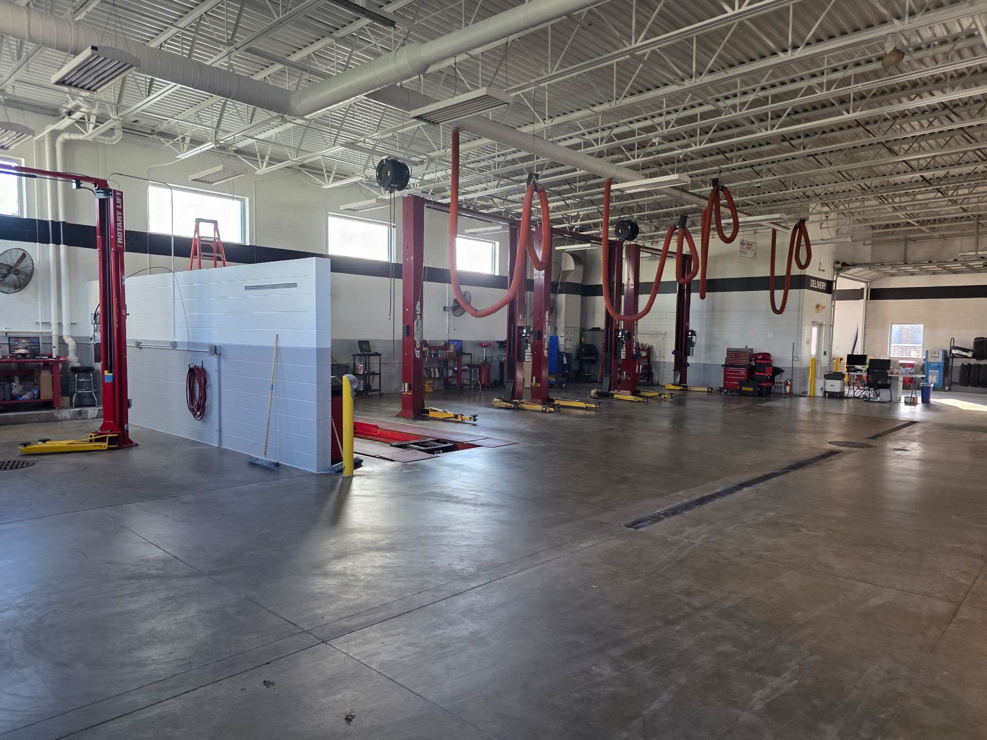 Interior of an auto repair shop with multiple red car lifts and equipment. Large, empty space with a concrete floor.