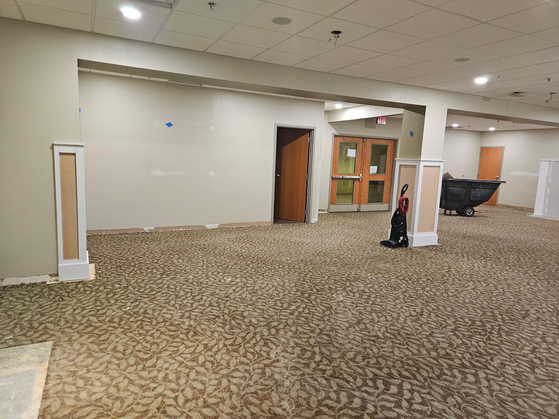 Room with tan carpet, beige walls, doorways, and unfinished pillar accents.