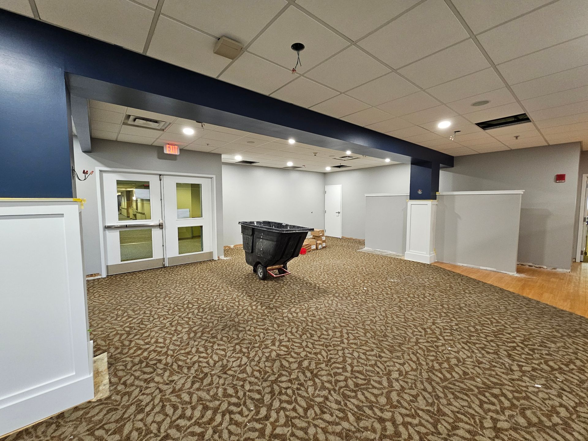 Interior room with new carpet, blue and grey walls, double doors, and a trash bin.