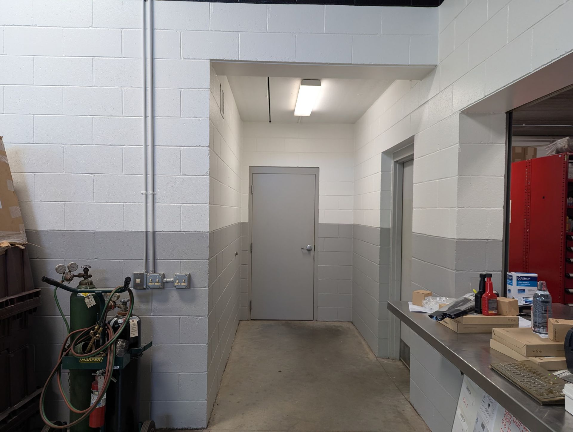 Hallway with gray-painted brick walls, a closed door, and industrial equipment visible on the left.