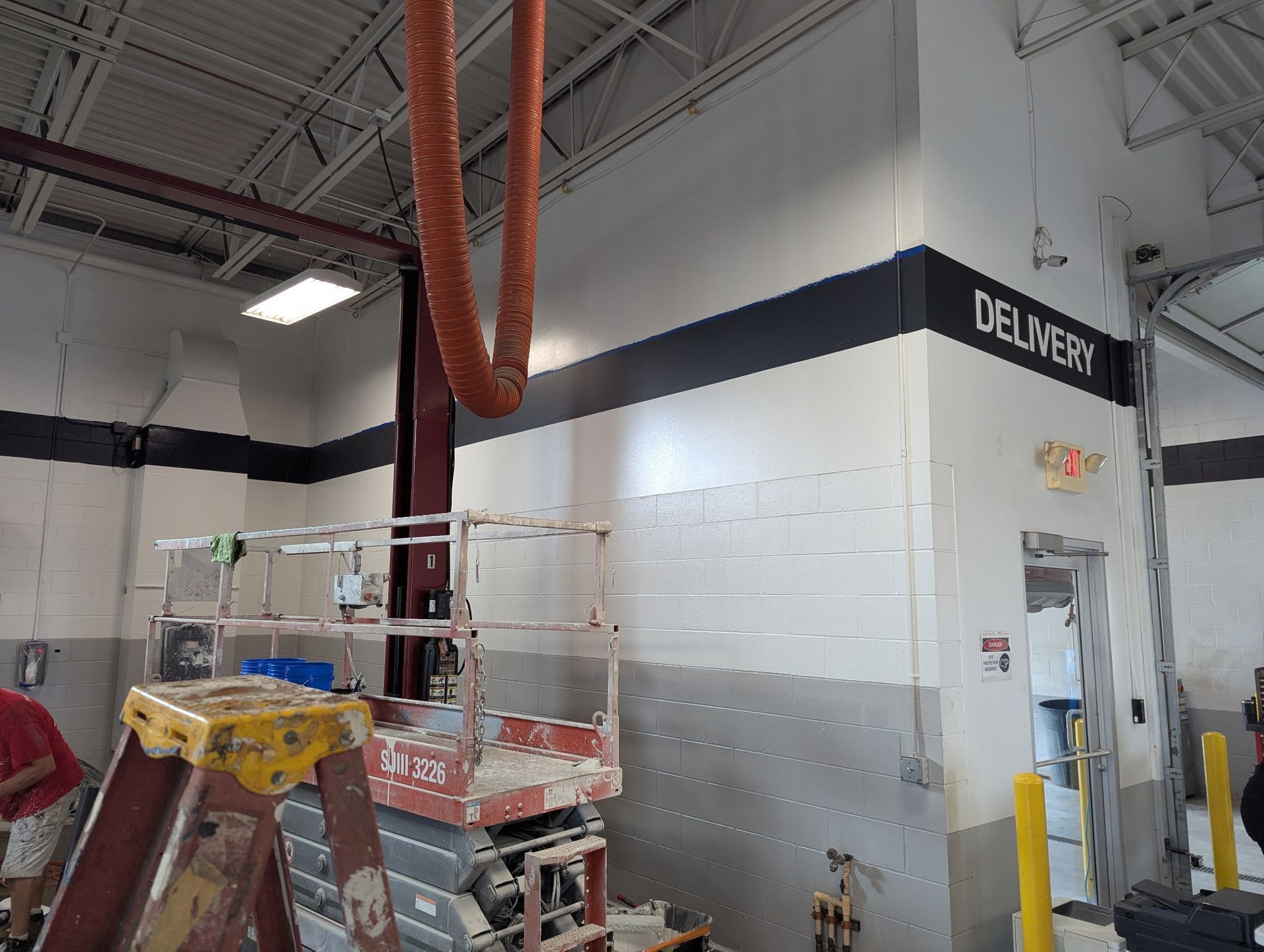 Interior view of a delivery area with signage on a white and gray wall, construction equipment in front.