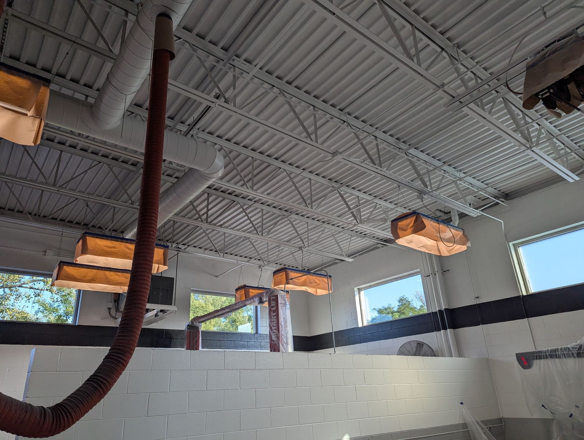 Interior view of a building under construction. White painted walls and ceiling with exposed metal beams. Brown ventilation.