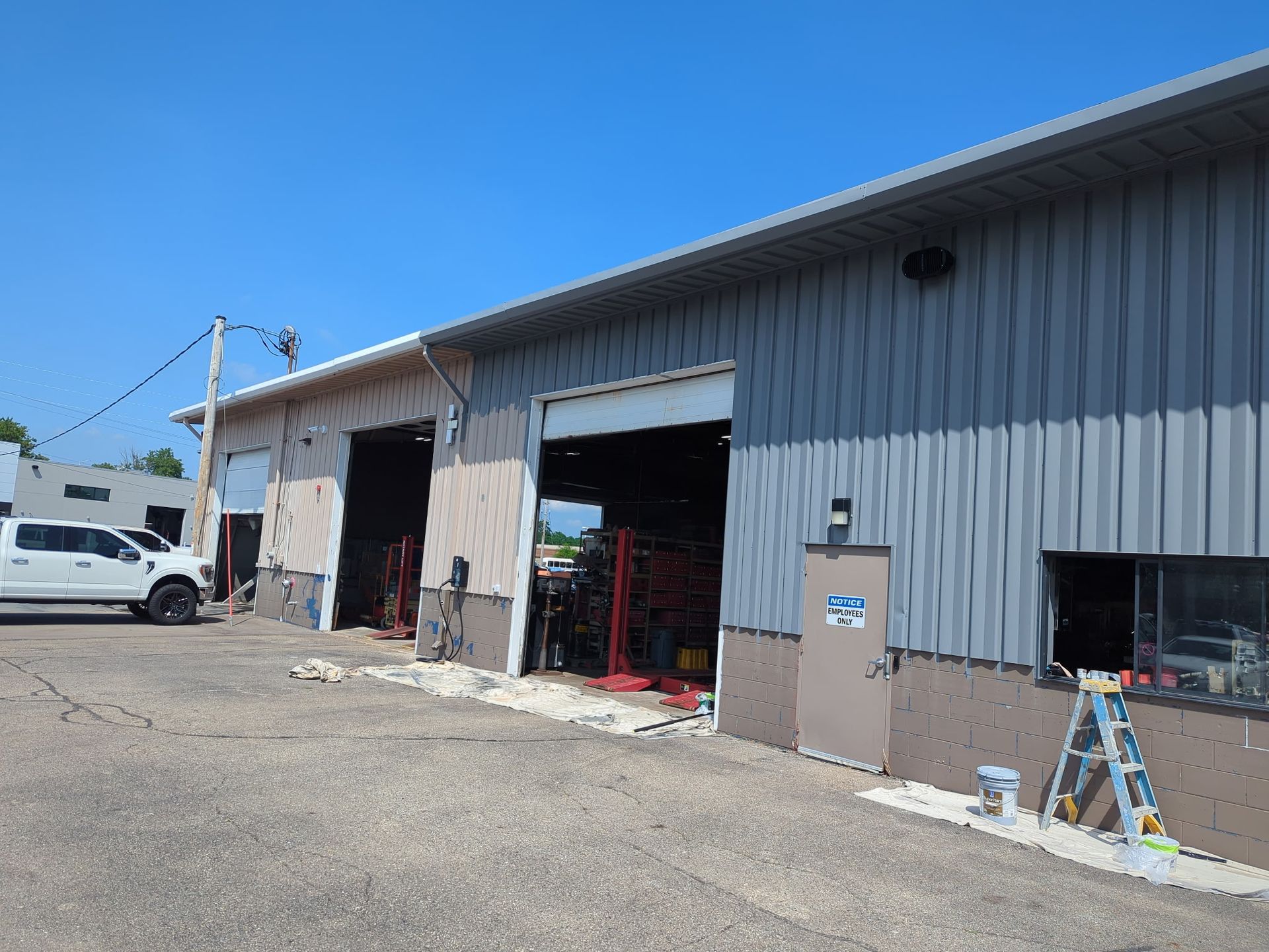 Exterior of a garage with open bays. Gray corrugated metal siding, truck parked, blue sky.