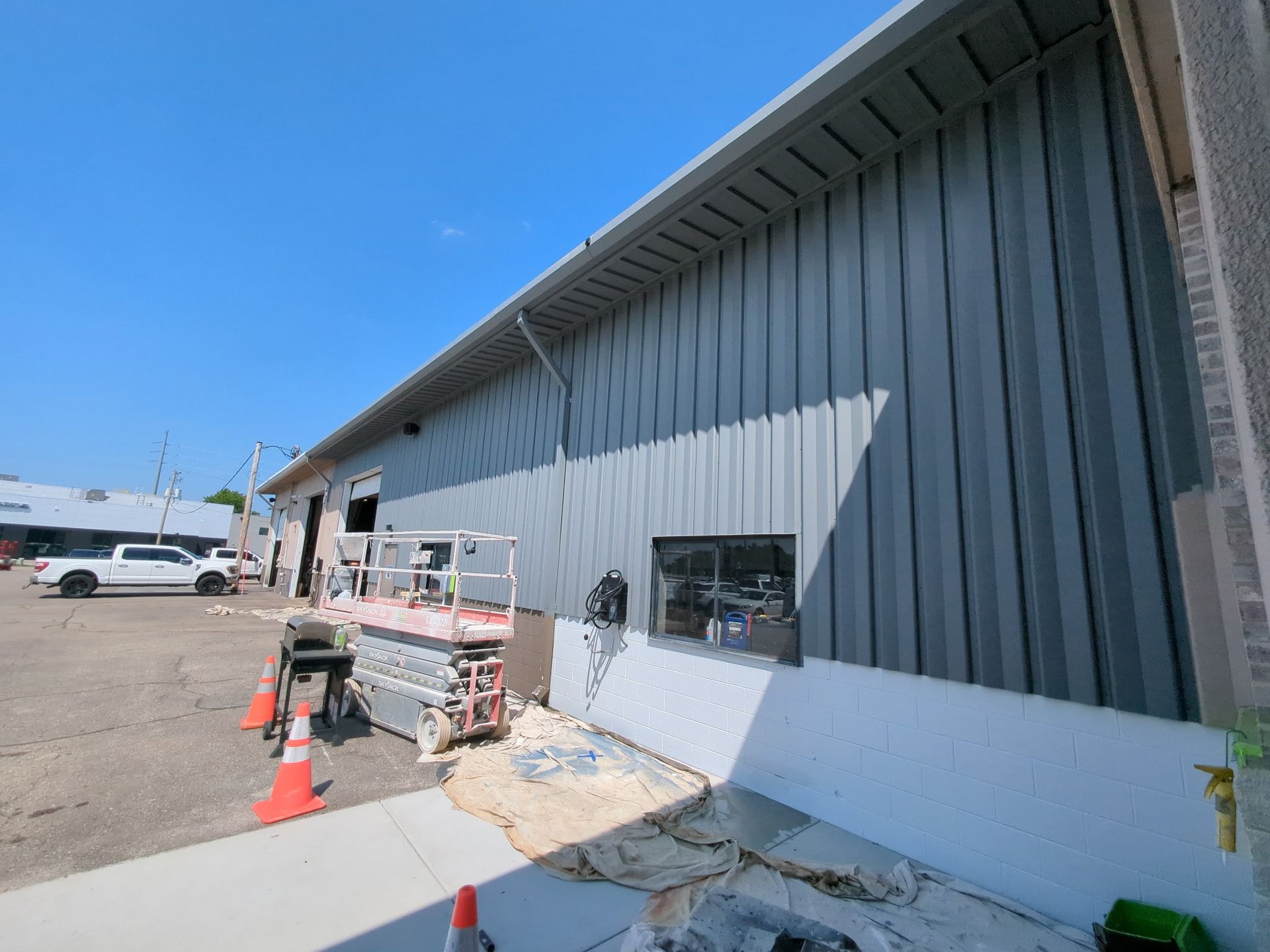 Building exterior under construction; gray metal siding, lift, white truck, blue sky.