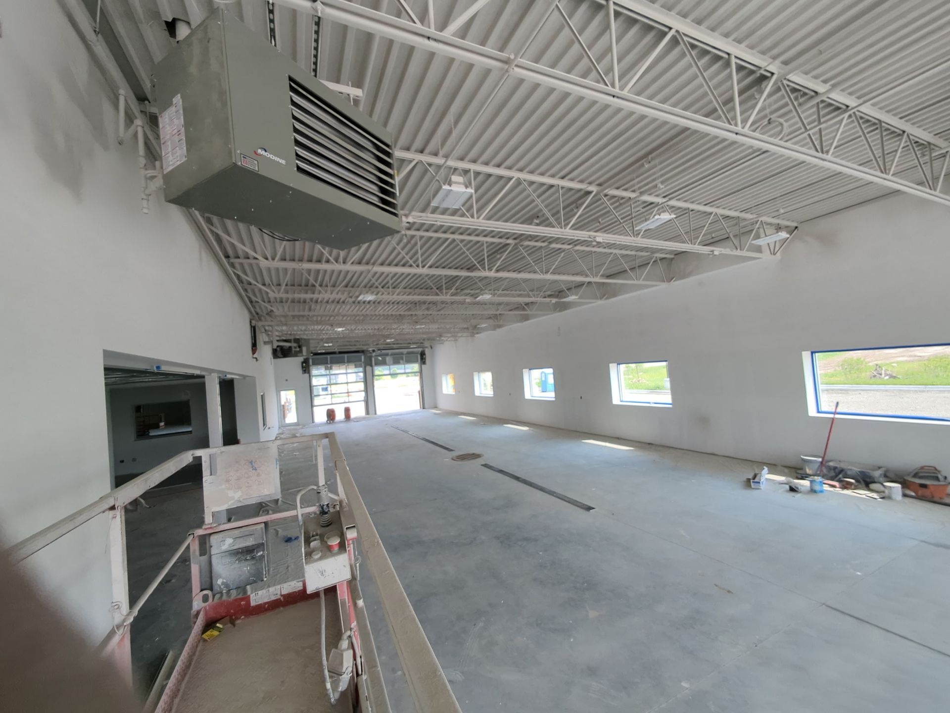 Interior of a large, unfinished commercial space with exposed ceiling trusses and a suspended heater.
