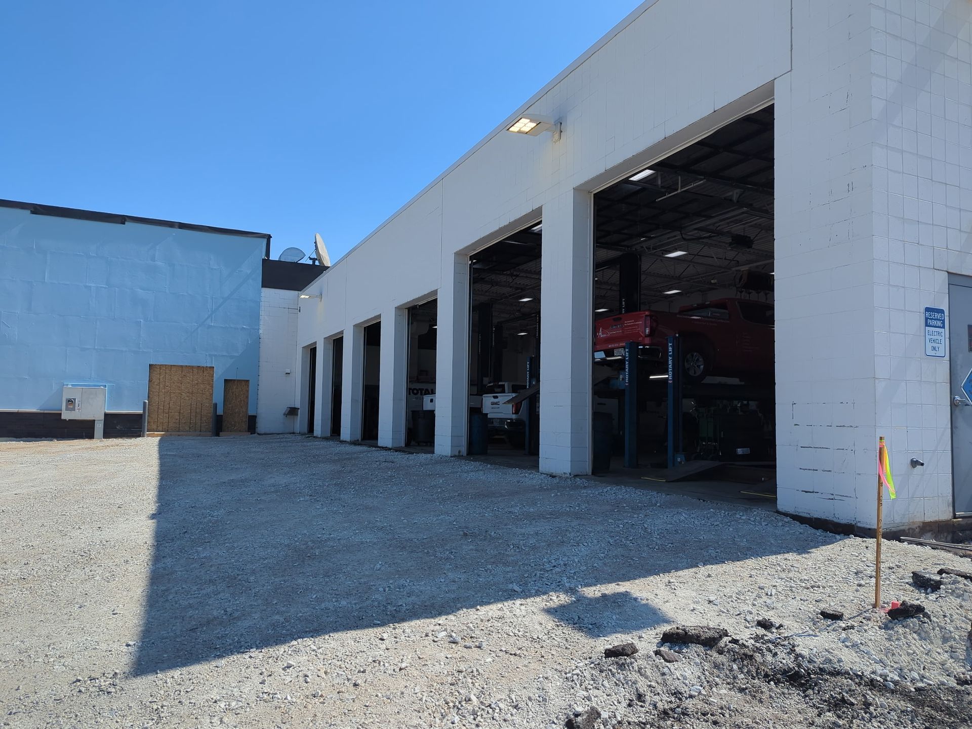 Exterior of a white auto repair shop with open garage doors; gravel lot. A blue building is adjacent.
