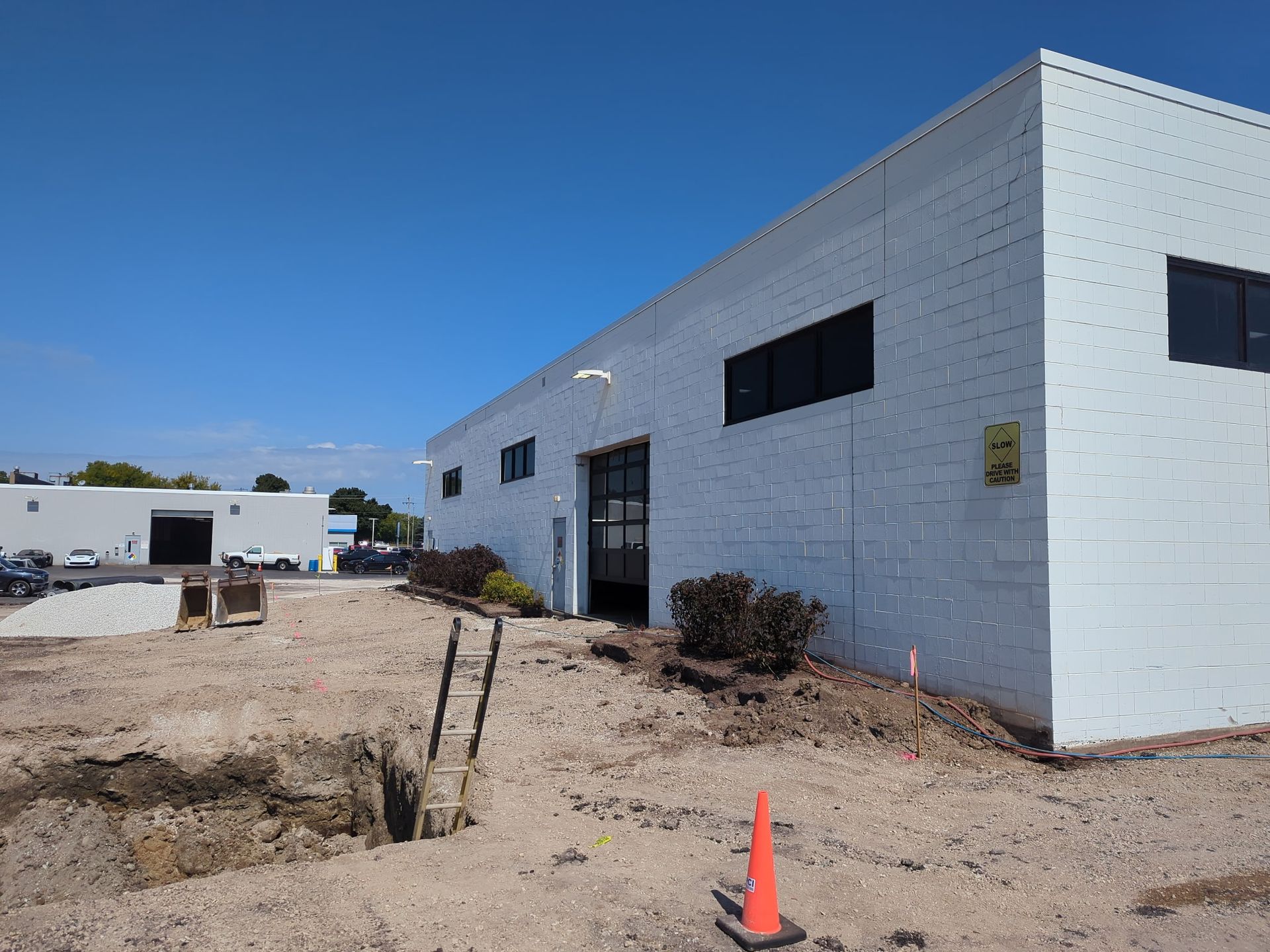 Exterior of a white brick building on a sunny day. Ground is dirt, with construction visible.