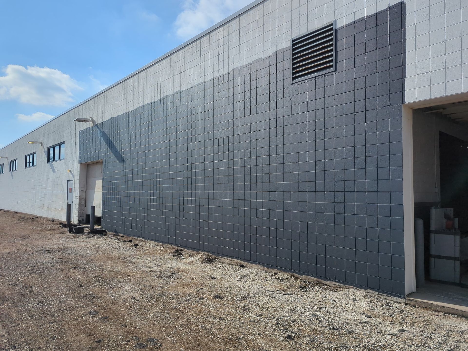 Exterior of a building with a textured dark gray paneling covering a portion of the wall, set against a blue sky.