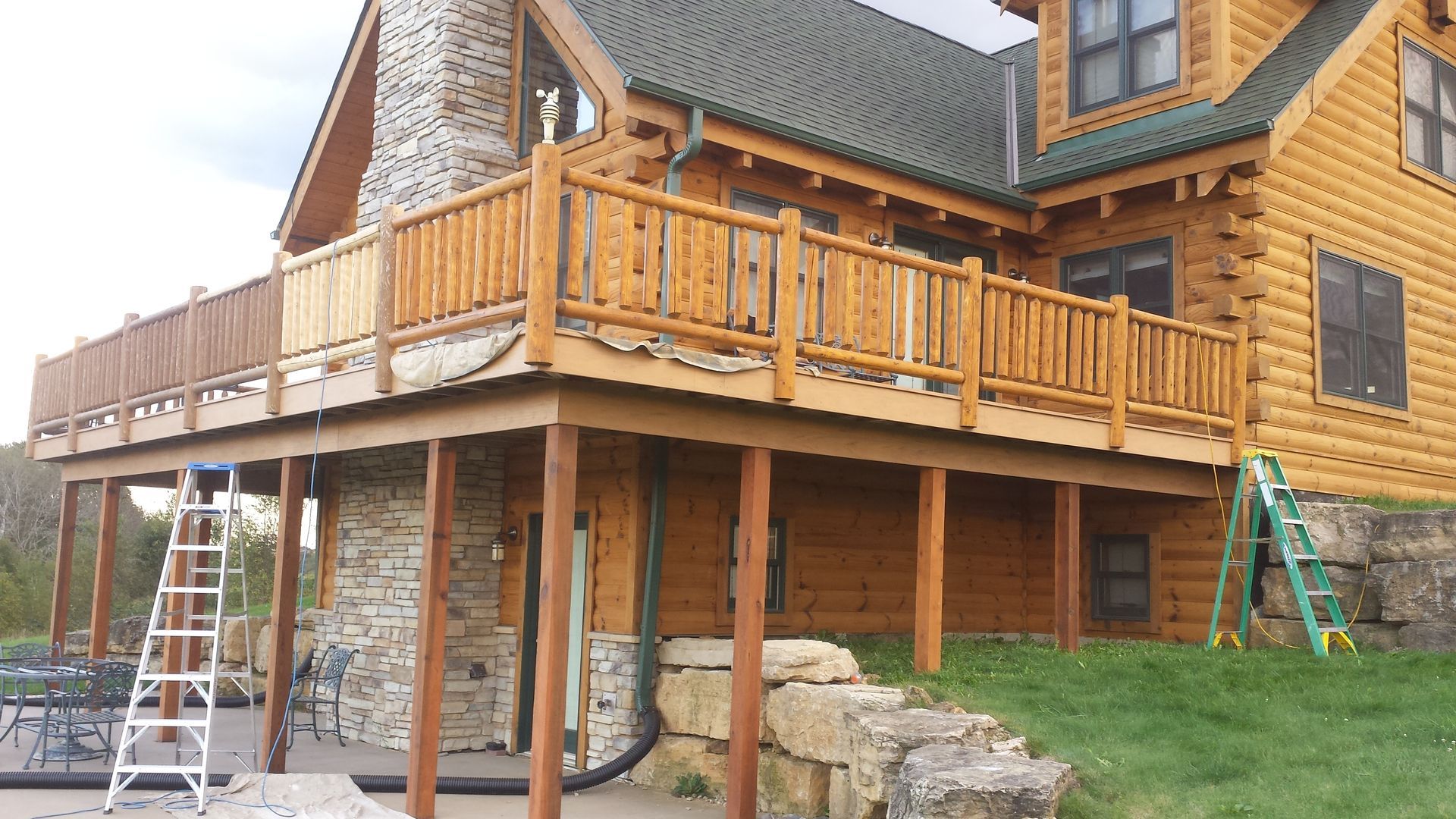 Log cabin with a wooden deck; a ladder leans against it.