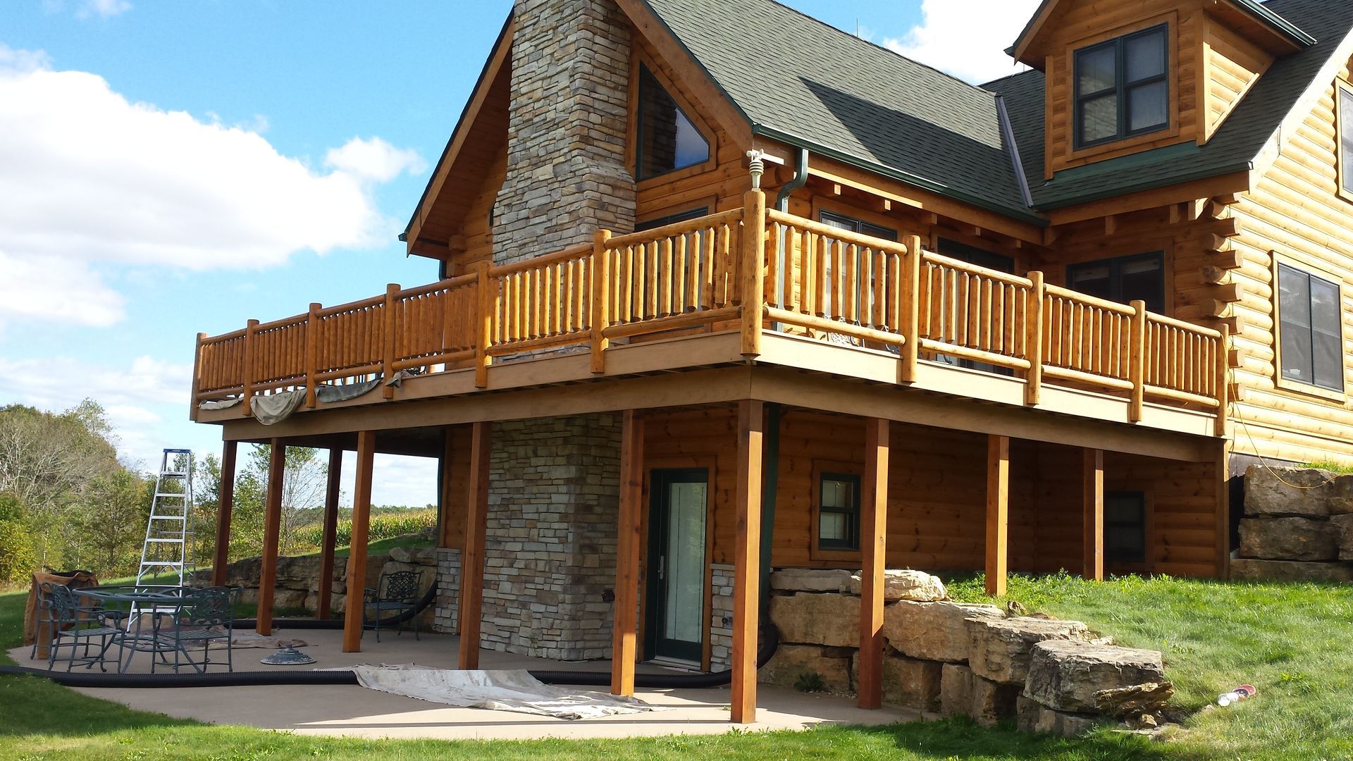 Wooden house with upper deck and stone accents on a grassy hill.