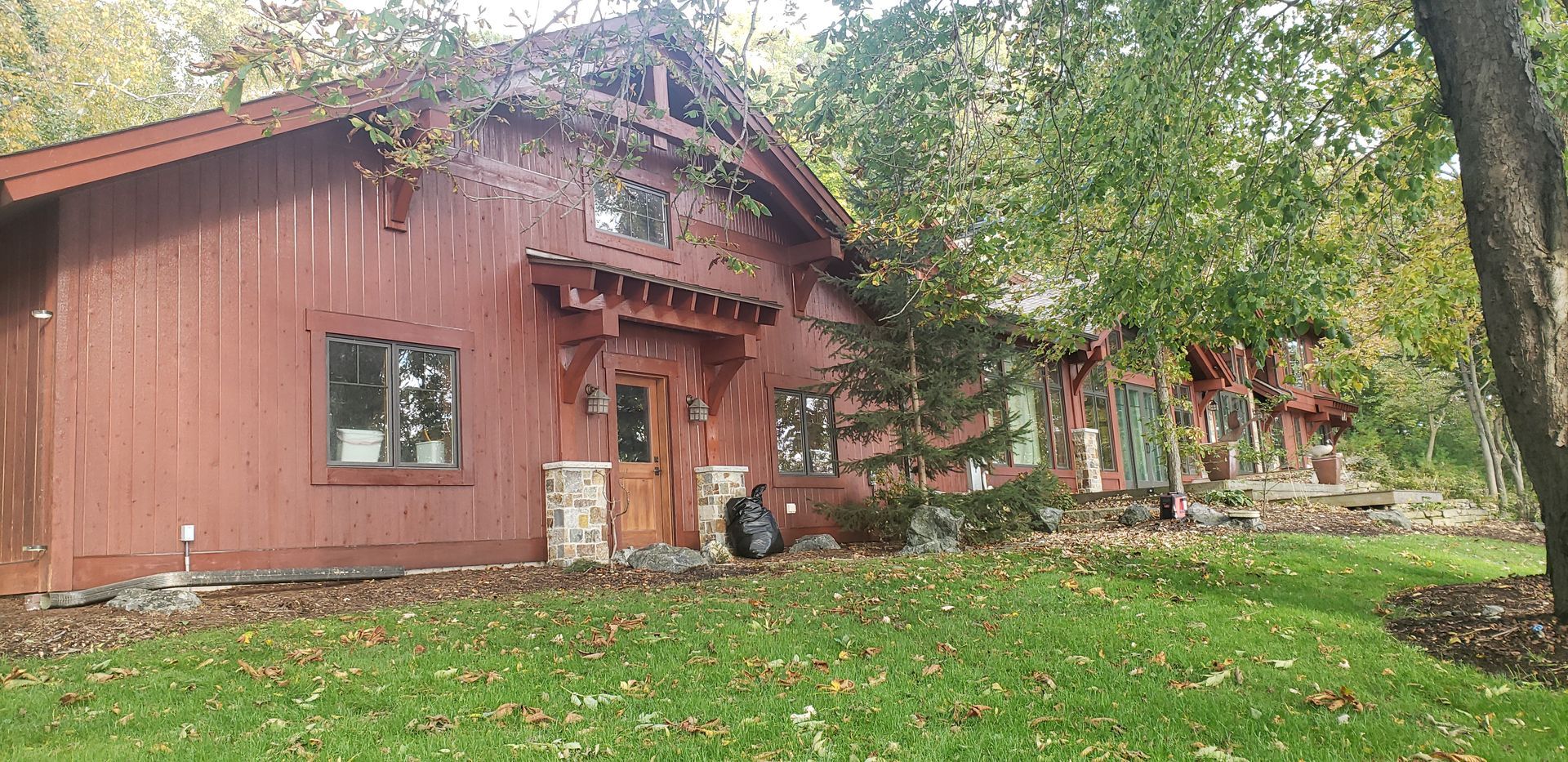 Red-sided building with stone pillars and wooden door, surrounded by green grass and trees.