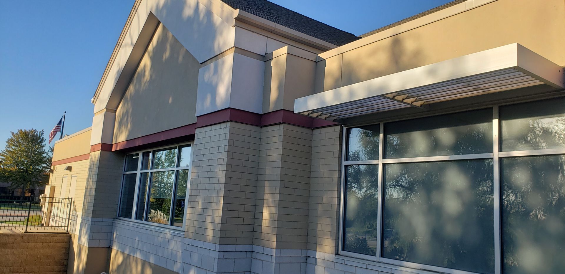 Building exterior with large windows, awning, and American flag on a sunny day.