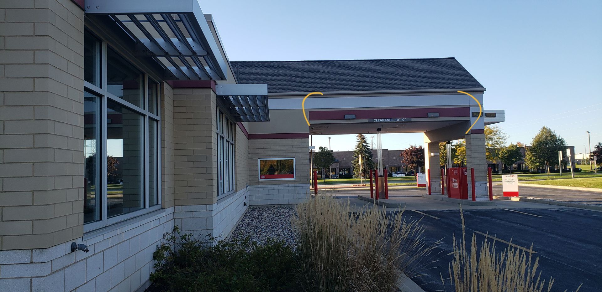 Bank drive-thru with red accents. Gray roof, tan brick building, with a blue sky background.