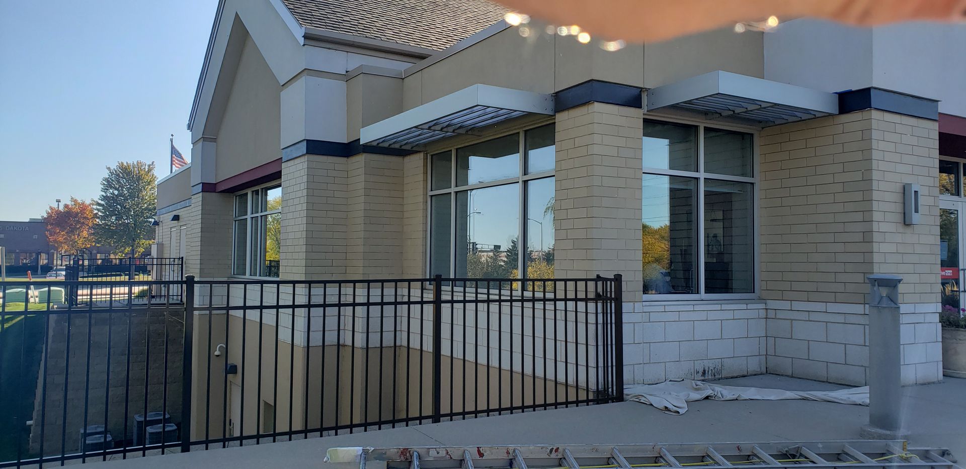 Exterior of a commercial building with brick facade, black metal fence, and windows.