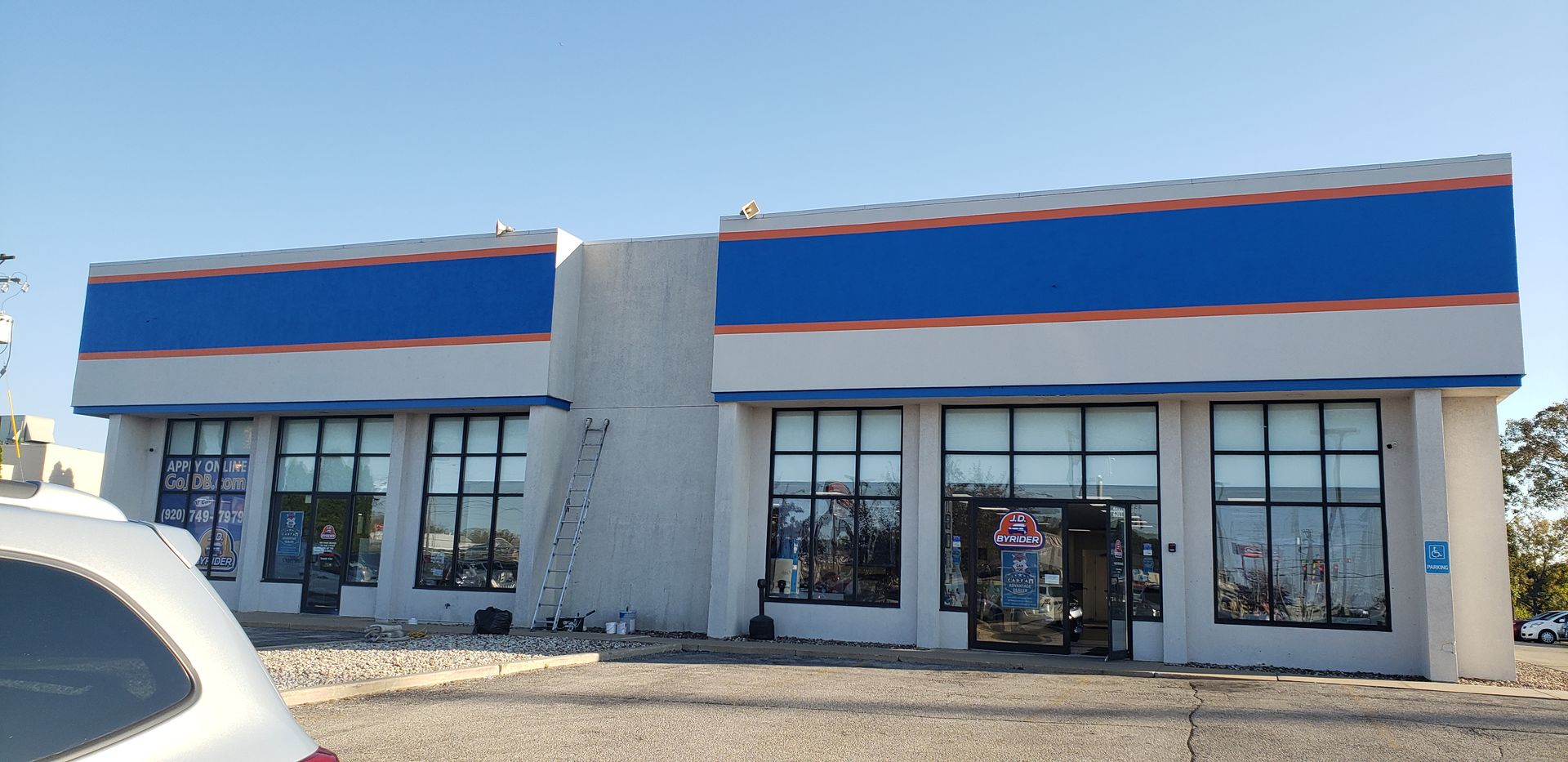 A two-story commercial building with blue and white stripes, glass windows, and a clear blue sky.