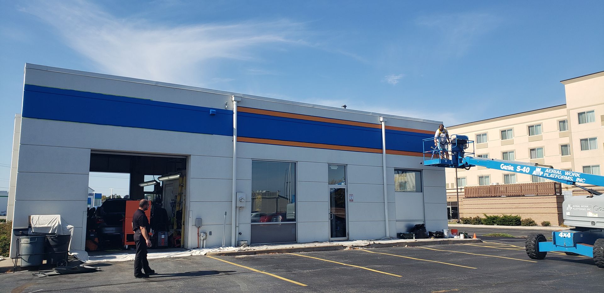 A building is painted blue and white. A worker in a lift is working on the building's facade.