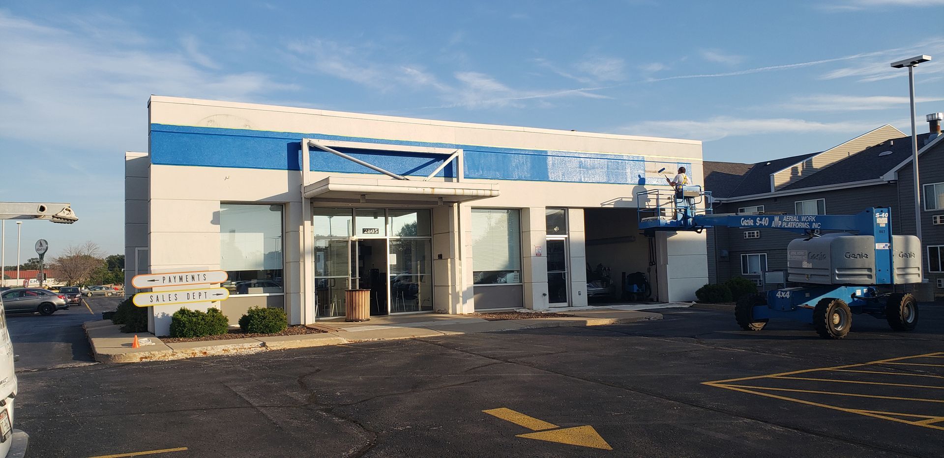 Exterior view of a building with blue and white accents. A blue lift is visible.