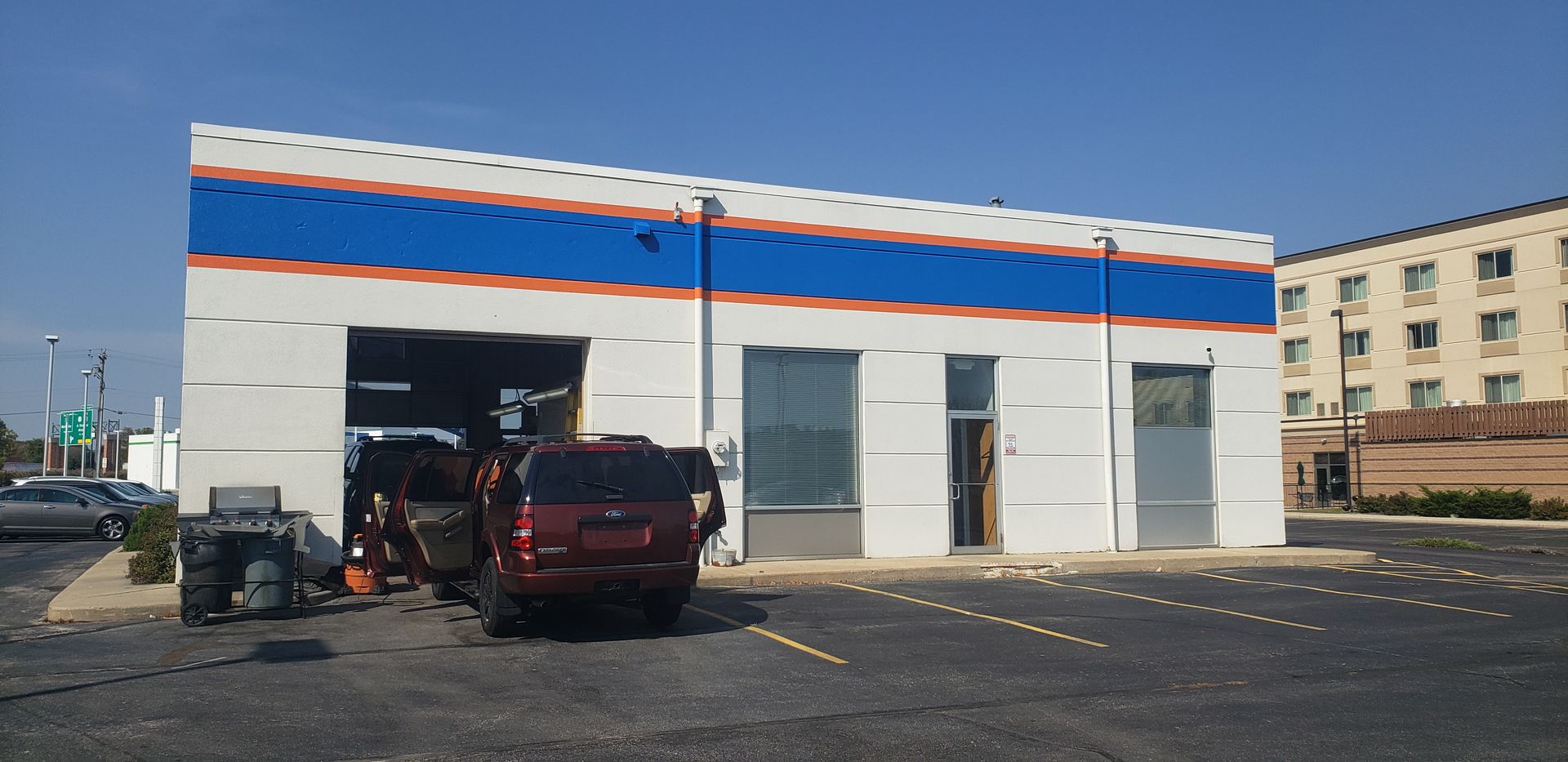 Exterior of a car wash facility with a car inside the bay. Blue and red trim, sunny day.