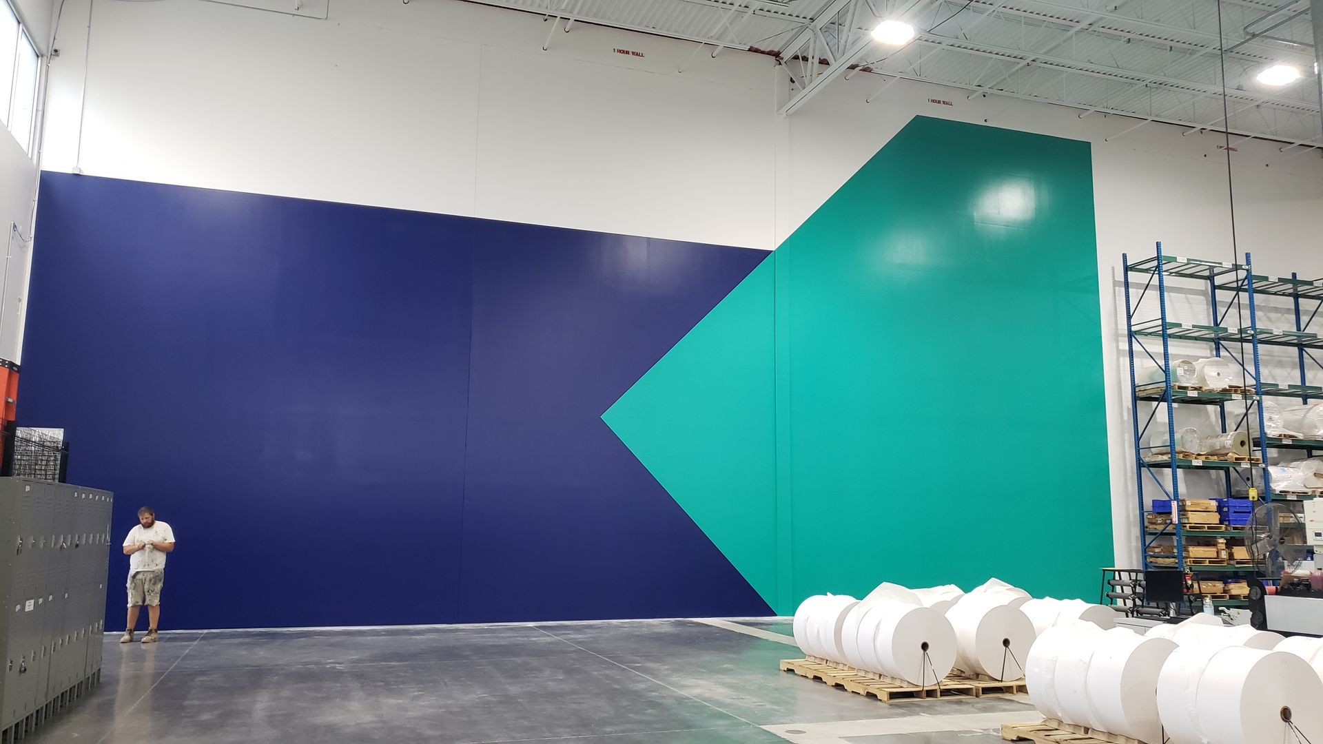 Large wall painted blue and teal, with a person standing in front of it in a warehouse setting.