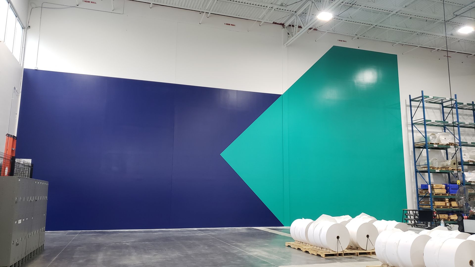 Blue and teal geometric design on an interior wall with rolls of paper on the floor.