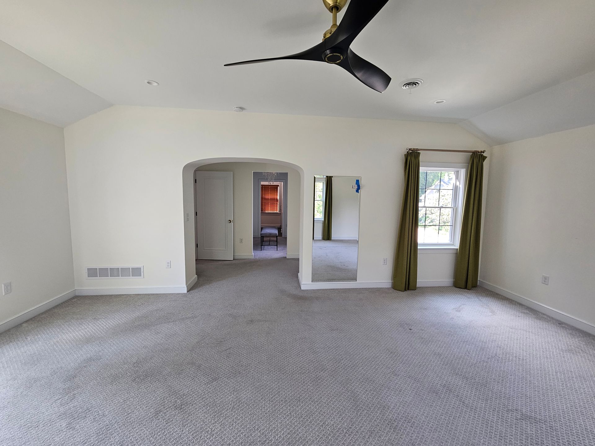 Empty bedroom with gray carpet, white walls, arched doorway, and a ceiling fan.