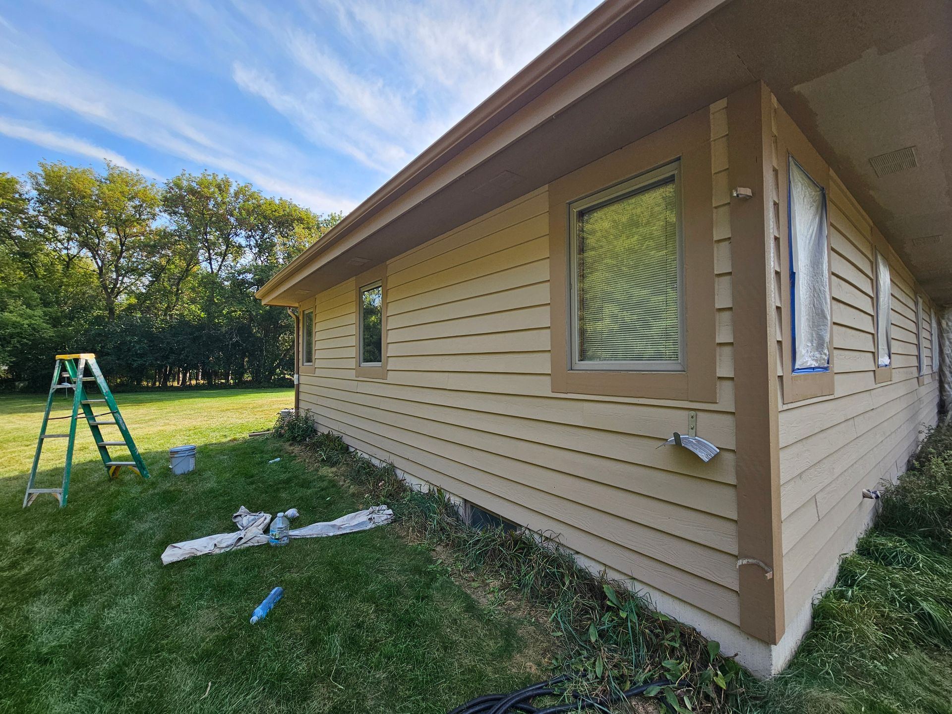 Beige house exterior with brown trim and windows, with a green ladder and lawn in the yard.