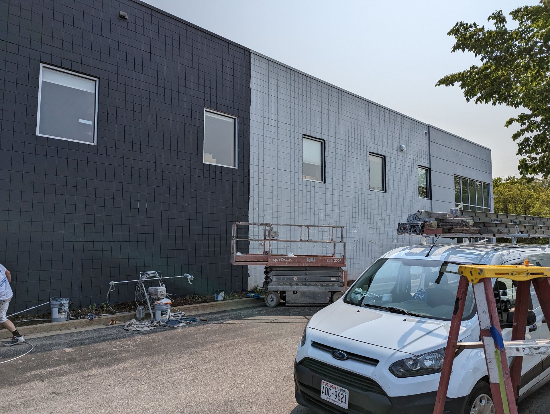 Exterior of a building, half black and half white, with a white van and construction equipment in front.