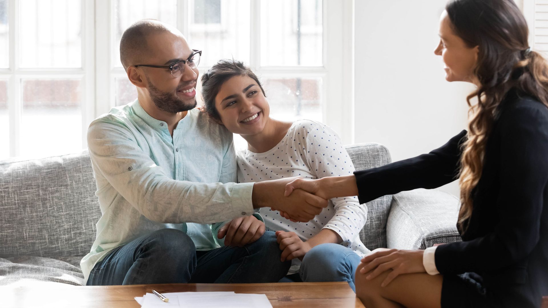 Couple shakes hands with a woman, smiling in a living room.