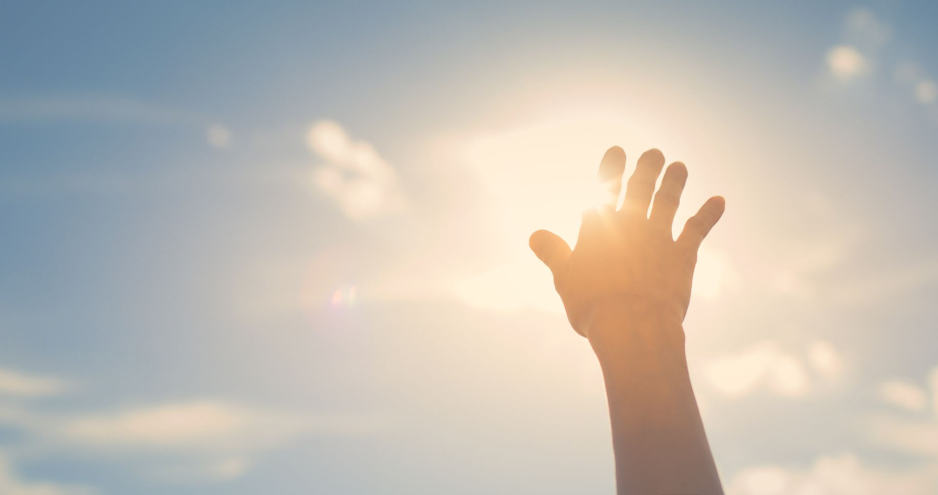 Hand reaching up toward the bright sun in a blue sky.