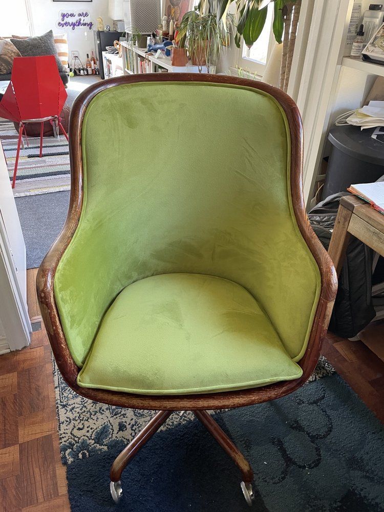 Lime green velvet chair with a wooden frame and a swiveling base, indoors.