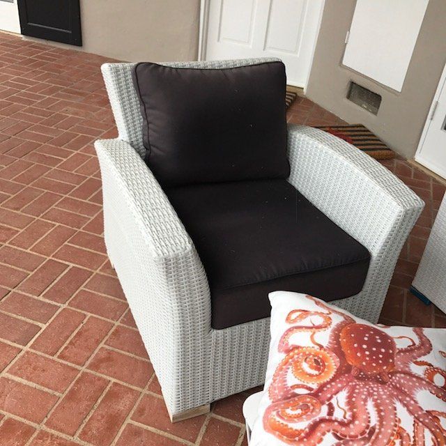 White wicker chair with brown cushions on a red brick patio, octopus pillow nearby.