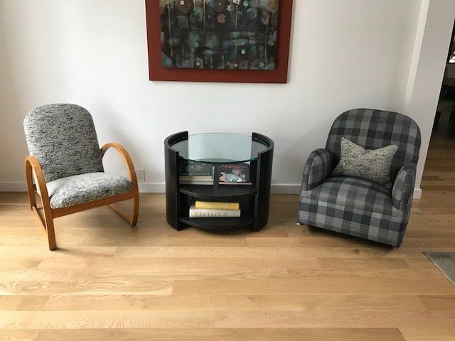 Two armchairs flanking a black table with glass top; art on wall; light wood floor.