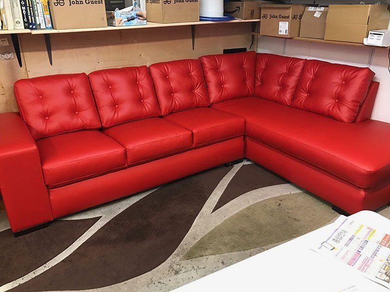 Red sectional sofa in a room with a patterned rug, shelves, and boxes.