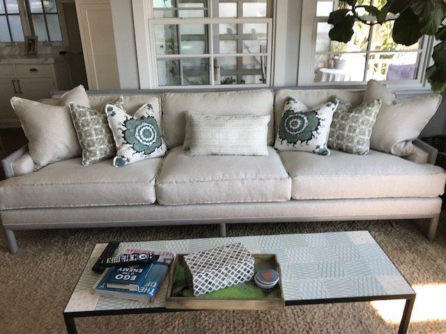 Beige sofa with multiple pillows, in a light-filled living room. A coffee table is in front of the sofa.