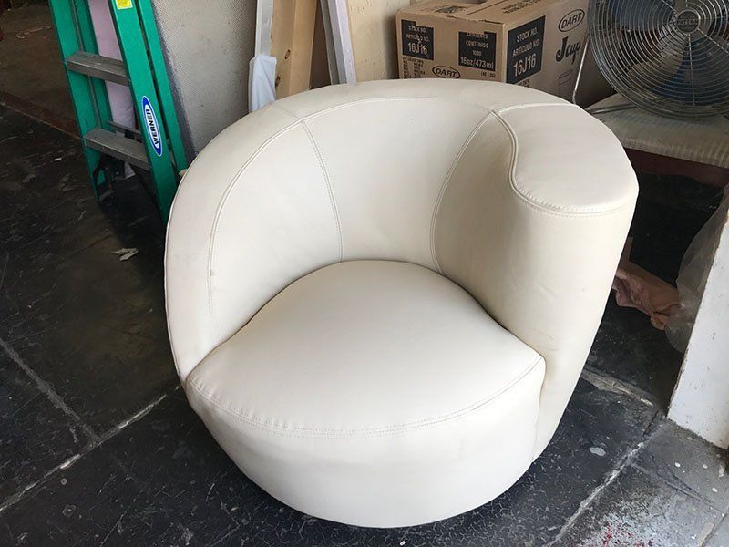 Off-white leather swivel chair in a workshop setting, with a ladder and fan in the background.
