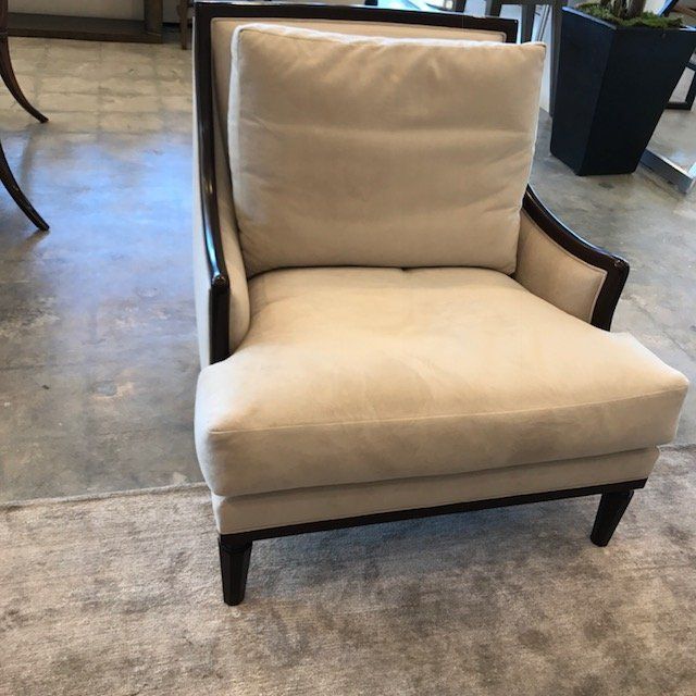 Cream-colored armchair with dark wooden frame and a matching cushion, on a patterned rug.
