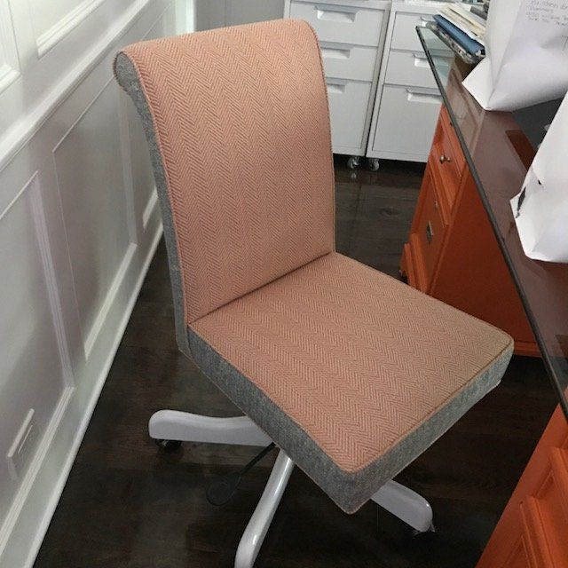 Pink and gray upholstered office chair with a white base, in front of a wall and desk.