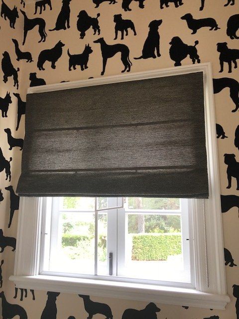 Gray roman shade over a white window with a view. Dog silhouette wallpaper surrounds it.