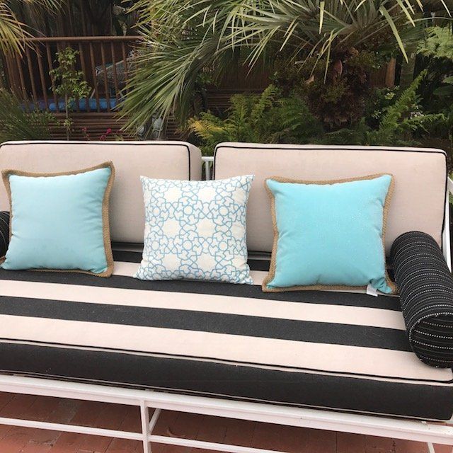 Outdoor sofa with turquoise and patterned pillows on a striped cushion, with palm trees in the background.