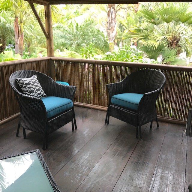 Two wicker chairs with blue cushions on a wooden deck, tropical foliage background.