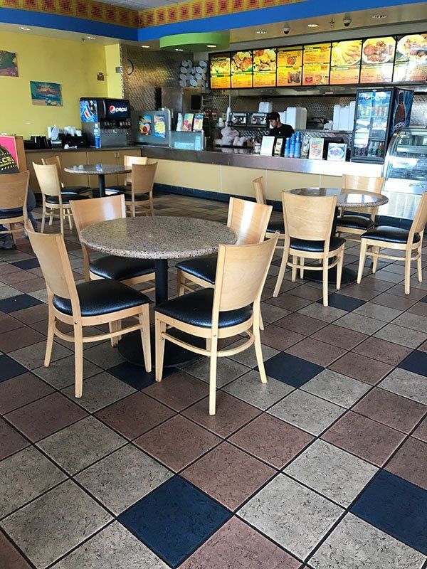 Interior of a fast food restaurant. Tables, chairs, counter with menu above. Colorful tile floor.