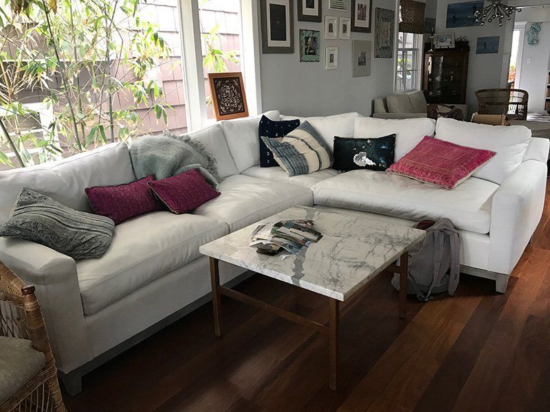 White sectional sofa with colorful pillows, next to a marble-topped coffee table in a bright room.