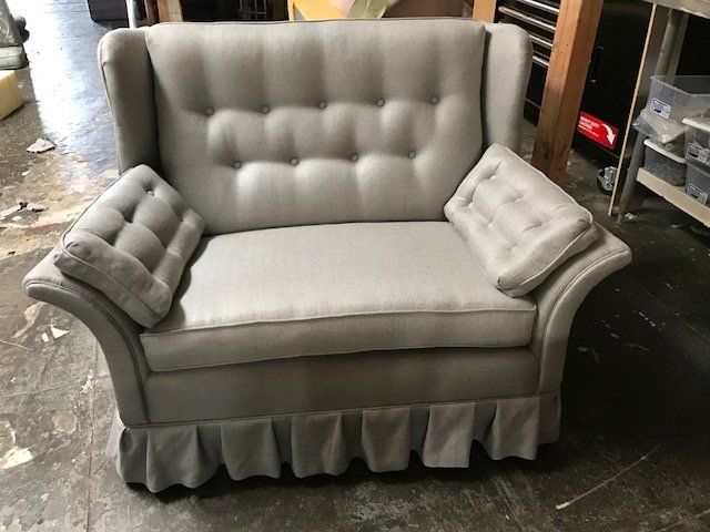 Gray upholstered loveseat with tufted back and arm pillows; pleated skirt base.