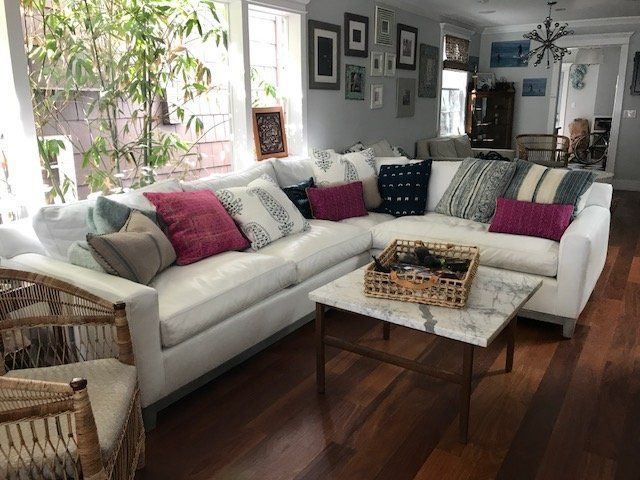 Living room with white sectional sofa, decorative pillows, marble coffee table, wood floor, and windows.