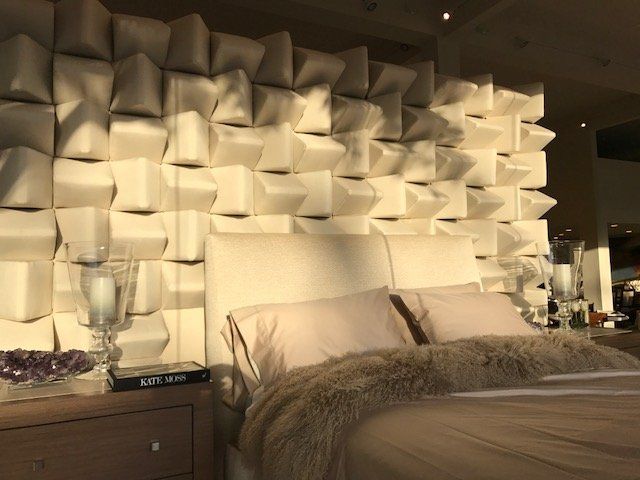 Bedroom with a textured white wall behind a bed with light-colored bedding and a faux fur throw.