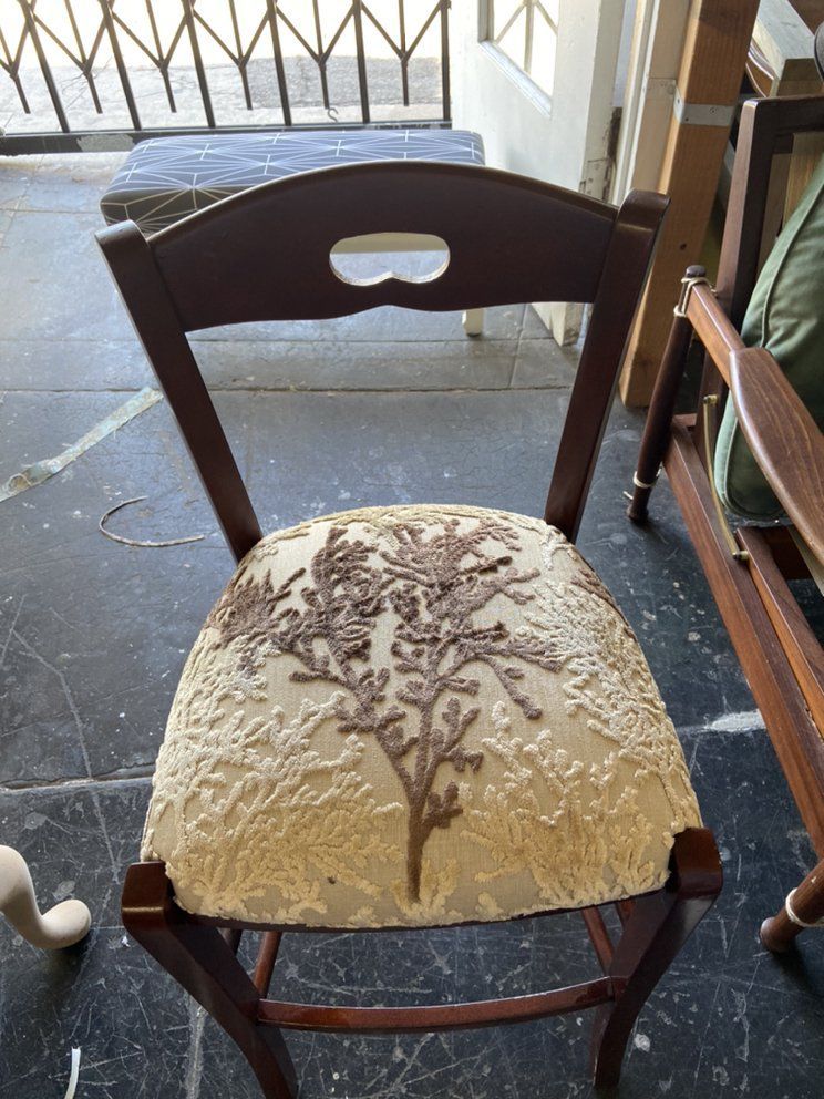 Wooden chair with upholstered seat, featuring brown embroidery, in a room.