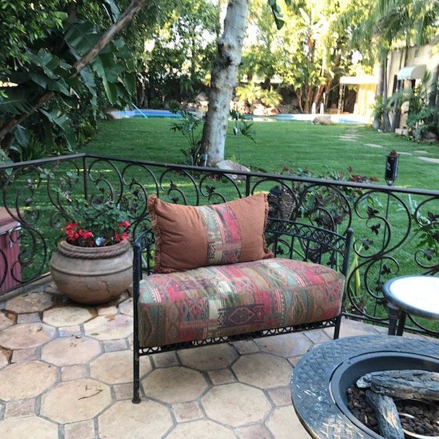 Wrought iron bench with patterned cushion on a tiled patio overlooking a green lawn.