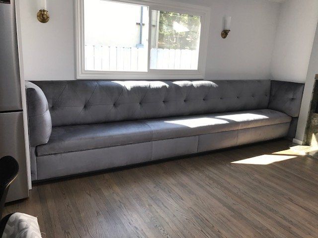 Gray, button-tufted banquette bench under a window in a bright room with hardwood floors.