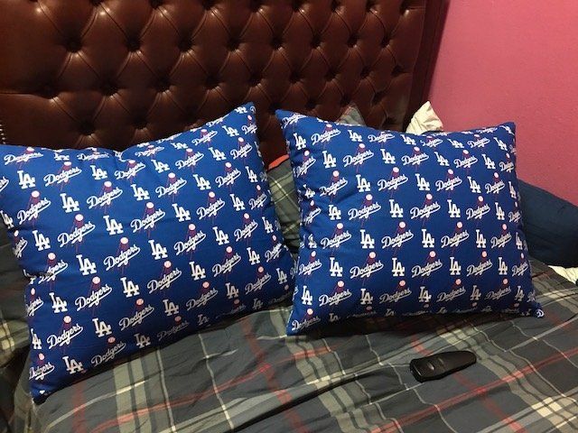 Two Dodger-themed pillows on a bed with a brown leather headboard and checkered bedspread.